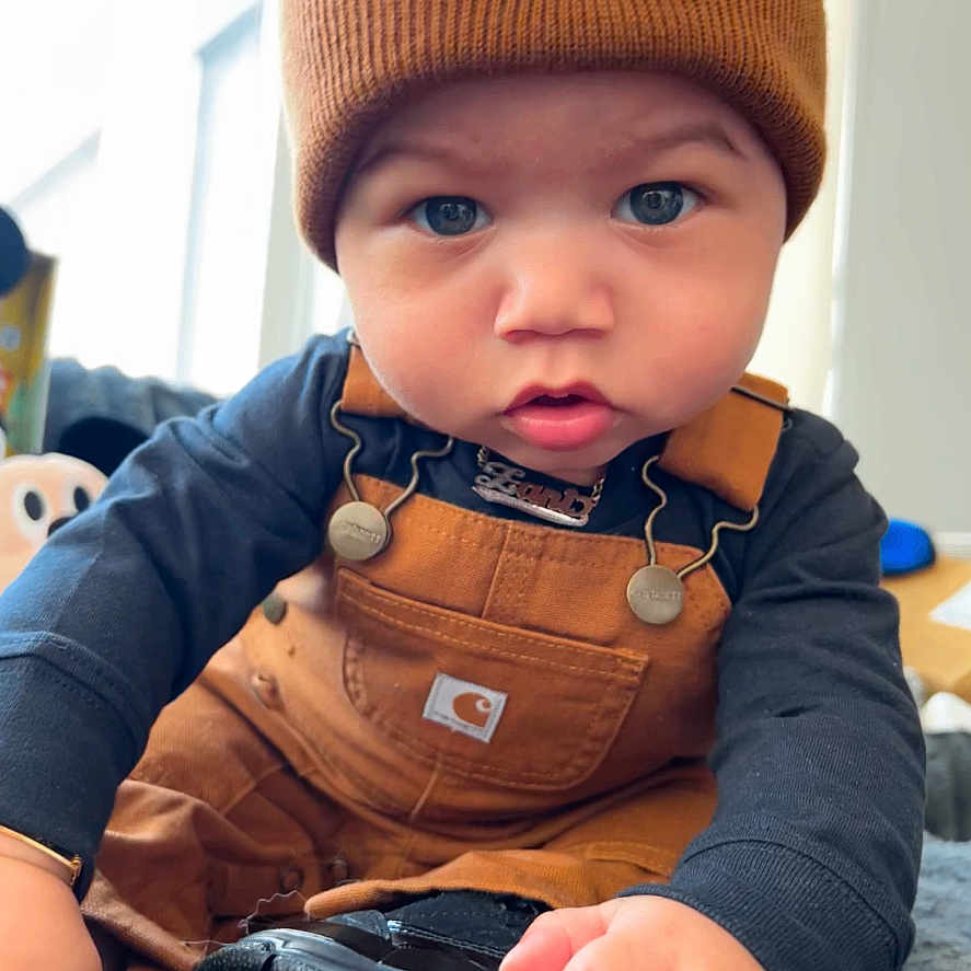 Zani is registered to the contest to win money with this photo: baby, beanie, black_shoe, blue_eyes, carhartt, child, closeup, clothing, curious, cute, face, hand, indoor, infant, jordan, overalls, portrait, sneaker, soft_light, warm_colors