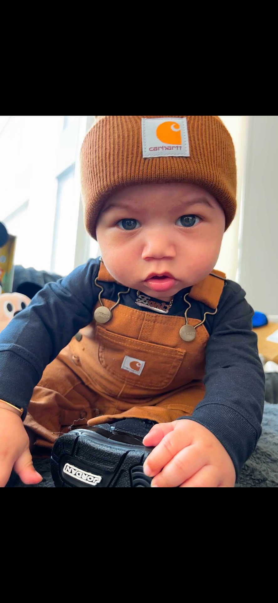 Zani is registered to the contest to win money with this photo: baby, child, face, beanie, carhartt, overalls, sneaker, jordan, hand, indoor, curious, blue_eyes, clothing, portrait, cute, infant, black_shoe, soft_light, closeup, warm_colors