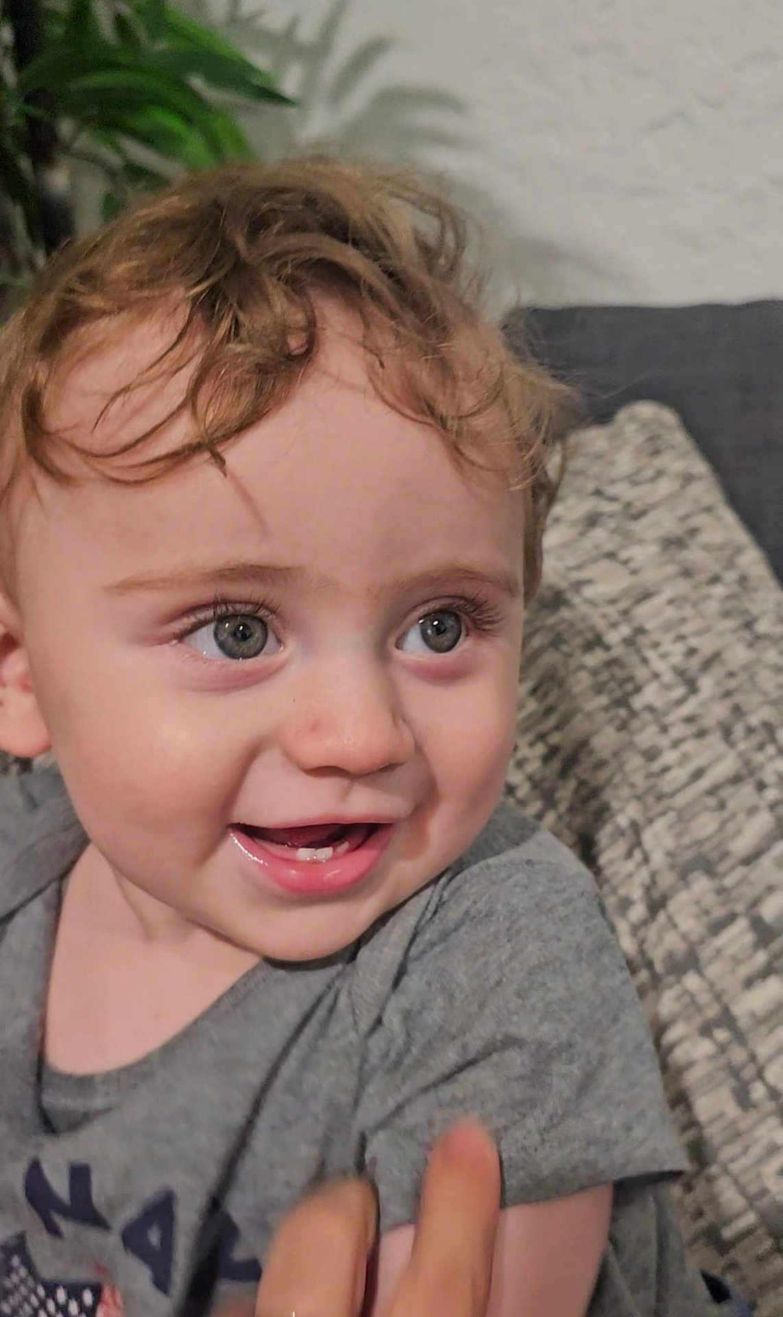 Yayan is registered to the contest to win money with this photo: toddler, child, smiling, curly_hair, face, eyes, couch, cushion, indoor, plant, person, happy, clothing, portrait, baby, skin, head, expression, young, casual