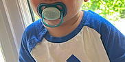 Maxime a rejoint le concours — aidez-le/la à gagner de superbes lots ! adidas_shirt, baby, blue_eyes, bottle, casual_clothing, child, closeup, curious, face, green_foliage, hand, indoor, natural_light, pacifier, person, portrait, short_hair, sitting, toddler, window