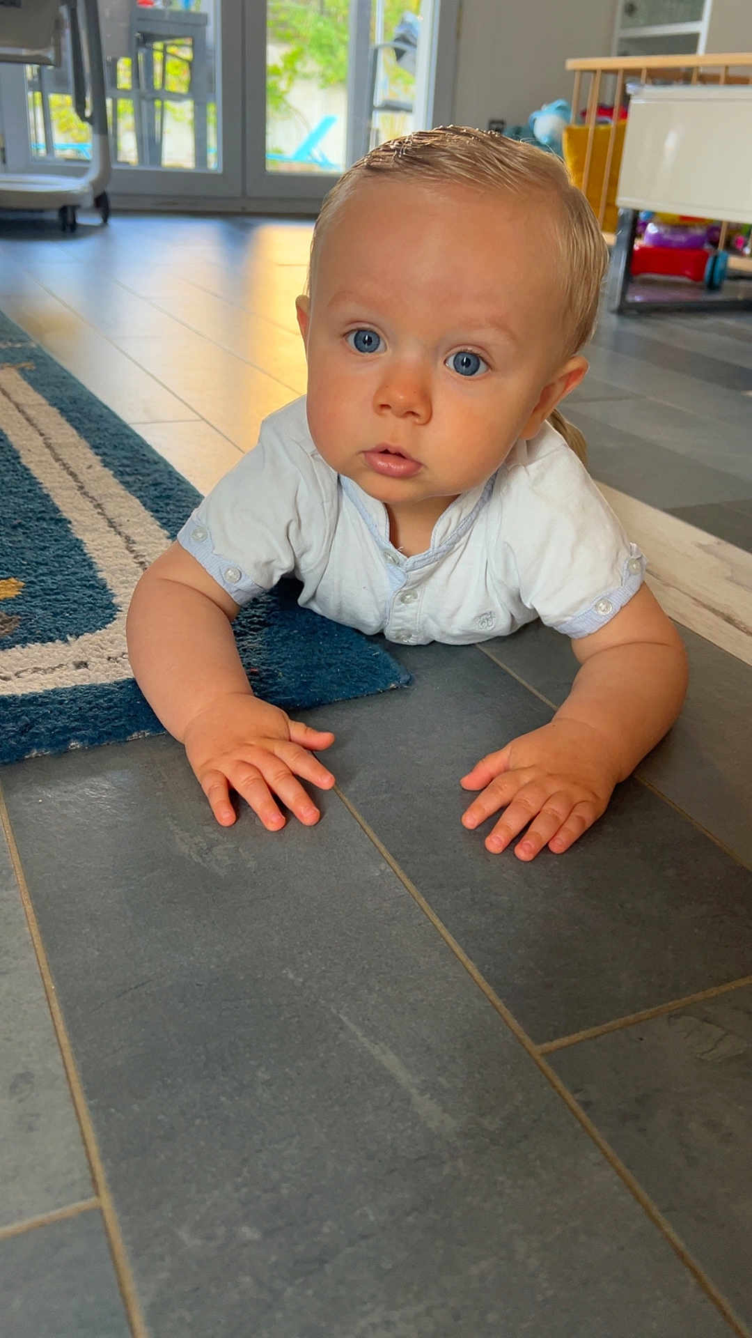 Maxime participe au concours pour gagner de l'argent avec cette photo : baby, child, indoor, floor, blue_eyes, curious, hands, shirt, tile_floor, rug, toy, home, crawling, person, young, infant, portrait, bright, looking, casual
