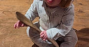 Billy is registered to the contest to win money with this photo: baby, child, toddler, sitting, indoors, kitchen, floor, wooden_floor, wooden_spoon, earmuffs, furry_earmuffs, gray_clothing, onesie, white_socks, cat, pet, cooking, pan, portrait, cute