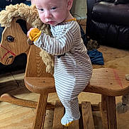 Billy joined the competition — help win amazing prizes! baby, child, rocking_horse, wooden_toy, striped_onesie, indoor, floor, person, furniture, leather_chair, toy, play, cute, young_child, wood, flooring, clothing, living_room, seated, contemplative