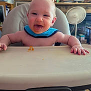 Billy joined the competition — help win amazing prizes! baby, infant, child, high_chair, smiling, tongue_out, portrait, indoor, home, feeding, food, tray, blue_bib, happy, sitting, face, hands, fan, television, rustic_interior