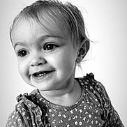 Mencïa participe au concours pour gagner de l'argent avec cette photo : child, toddler, portrait, black_and_white, smiling, happy, face, eyes, dress, pattern, ruffles, young_child, cute, innocence, joyful, clothing, baby, person, studio, closeup