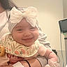 Amila is registered to the contest to win money with this photo: arm, baby, bib, bow, child, closeup, clothing, cute, face, happy, headband, holding, hospital, indoor, infant, medical_equipment, person, skin, smile, wristband