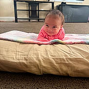Amila is registered to the contest to win money with this photo: baby, blanket, candle, carpet, child, cozy, curtains, cushion, face, floor, home, indoor, infant, lying_down, pink_clothing, plant, portrait, shelf, smiling, young_child