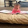 baby, blanket, candle, carpet, child, cozy, curtains, cushion, face, floor, home, indoor, infant, lying_down, pink_clothing, plant, portrait, shelf, smiling, young_child