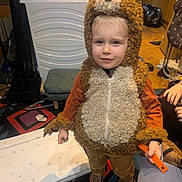 Reuben joined the competition — help win amazing prizes! bear_costume, brown, carpet, child, clothing, costume, face, footwear, furniture, hand, home, indoor, orange, patterned_rug, person, playful, smile, toy, young_child, zipper