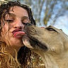 woman, dog, tongue, kiss, close_up, outdoor, smiling, curly_hair, light, face, pet, affection, nature, daylight, happy, expression, nose_ring, skin, animal, friendship