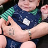 baby, child, infant, overalls, hat, camo, striped_shirt, hand, tattoo, wristwatch, smile, sitting, cute, person, clothing, indoor, comfort, skin, face, arm