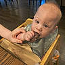 Heston joined the competition — help win amazing prizes! baby, child, high_chair, food, hand, indoor, wooden_furniture, curious, mohawk, bib, table, person, eating, meal, infant, cute, skin, face, eyes, holding