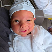 Mattéo a rejoint le concours — aidez-le/la à gagner de superbes lots ! baby, infant, face, hat, white_clothing, smile, cute, newborn, person, portrait, indoors, cozy, soft_texture, star_pattern, headwear, skin, expression, warmth, comfort, closeup