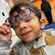 Isaac is registered to the contest to win money with this photo: child, glasses, smile, fleece, indoor, person, hand, face, sleeve, pattern, background, adult, jacket, orange_wall, window, playful, young, cozy, casual, portrait