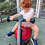 child, toddler, curly_hair, playground, spring_rider, red_seat, blue_sneakers, marvel, white_shirt, shorts, outdoor, fence, greenery, grass, play_equipment, toy, summer, daylight, person, focused