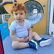 Sandro a rejoint le concours — aidez-le/la à gagner de superbes lots ! toddler, child, red_hair, white_shirt, blue_sneakers, marvel, playground, play_equipment, outdoor, sitting, curly_hair, window, thoughtful, casual_clothing, daylight, metal_structure, plastic_surface, fence, person, young_child