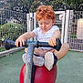 toddler, child, curly_hair, white_tshirt, playground, scooter, red_scooter, outdoor, greenery, fence, shoes, play, summer, daylight, park, young_child, toy, recreation, happy, casual_clothing