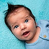 Eden is registered to the contest to win money with this photo: baby, infant, child, portrait, close_up, face, eyes, wide_eyed, smiling, lying_down, blanket, turquoise, blue, clothing, onesie, button, indoor, cozy, adorable, photography