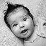 baby, child, infant, portrait, black_and_white, smiling, wide_eyed, lying_down, blanket, textured_fabric, indoors, close_up, face, eyes, hair, open_mouth, clothing, button, soft_lighting, photography