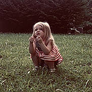 Mae is registered to the contest to win money with this photo: child, girl, grass, outdoor, nature, leaf, dress, summer, crouching, curly_hair, cute, young, portrait, daylight, greenery, yard, casual, exploring, person, feet
