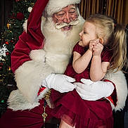 Mae is registered to the contest to win money with this photo: child, santa_claus, christmas_tree, holiday, festive, red_dress, white_beard, glasses, gloves, smiling, decorations, celebration, indoor, portrait, happy, toddler, christmas_lights, seasonal, family, joy