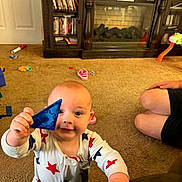 Koda is registered to the contest to win money with this photo: baby, child, toy, indoor, carpet, fireplace, furniture, person, onesie, hand, face, smile, adult, legs, living_room, sitting, play, curious, star_pattern, blue_toy