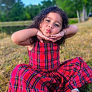 Alice Sofía joined the competition — help win amazing prizes! child, girl, red_dress, plaid, outdoor, grass, smiling, posing, sitting, playful, curly_hair, nature, daylight, footwear, sandals, greenery, fun, portrait, cute, happy