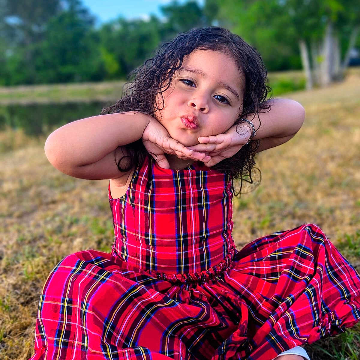 Alice Sofía joined the competition — help win amazing prizes! child, girl, red_dress, plaid, outdoor, grass, smiling, posing, sitting, playful, curly_hair, nature, daylight, footwear, sandals, greenery, fun, portrait, cute, happy