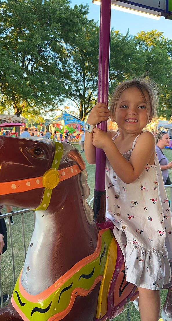 Brooklynn is registered to the contest to win money with this photo: baby_toddler_clothing, city, event, fun, happy, horse_tack, human_settlement, joy, leisure, outdoor_play_equipment, person, photograph, pink, playground, pole, recreation, smile, summer, toddler, tree