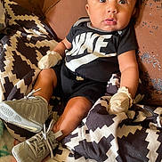 Kirk Jr is registered to the contest to win money with this photo: baby, infant, nike, clothing, sneakers, mittens, blanket, couch, leather, patterned, black_shirt, cute, portrait, indoor, child, young, sitting, wide_eyes, curious, comfortable