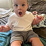 Brayden is registered to the contest to win money with this photo: baby, bed, blanket, casual_clothing, child, couch, cute, expression, face, gray_shorts, home, indoor, infant, person, sitting, skin, surprised, toy, white_tshirt, young_child