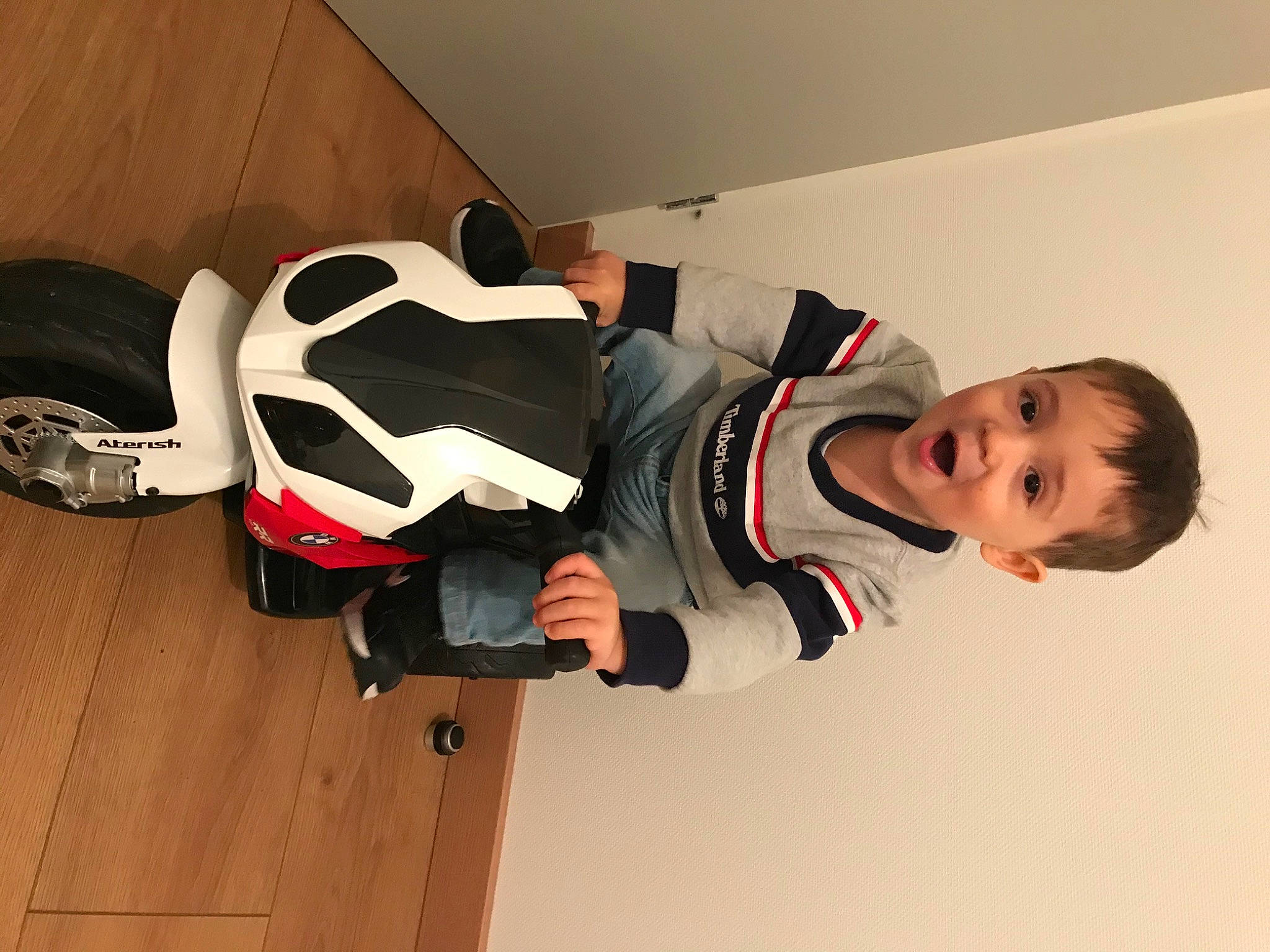 Tiago participe au concours pour gagner de l'argent avec cette photo : carmine, ceiling, flooring, hardwood, orange, person, personal_protective_equipment, rim, room, smile, surprise, toddler, vehicle, walking_shoe, wood