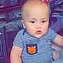baby, child, striped_shirt, tiger_patch, holding, arm, indoor, television, dvd, poster, photo_collage, furniture, person, casual_clothing, cute, chubby_cheeks, home, relaxed, seated, light