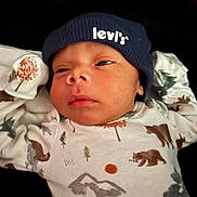 Zyion is registered to the contest to win money with this photo: baby, infant, beanie, hat, clothing, onesie, forest_pattern, animal_print, bear, tree, mountain, red_sun, closeup, face, headwear, sleepy, cute, newborn, portrait, indoor