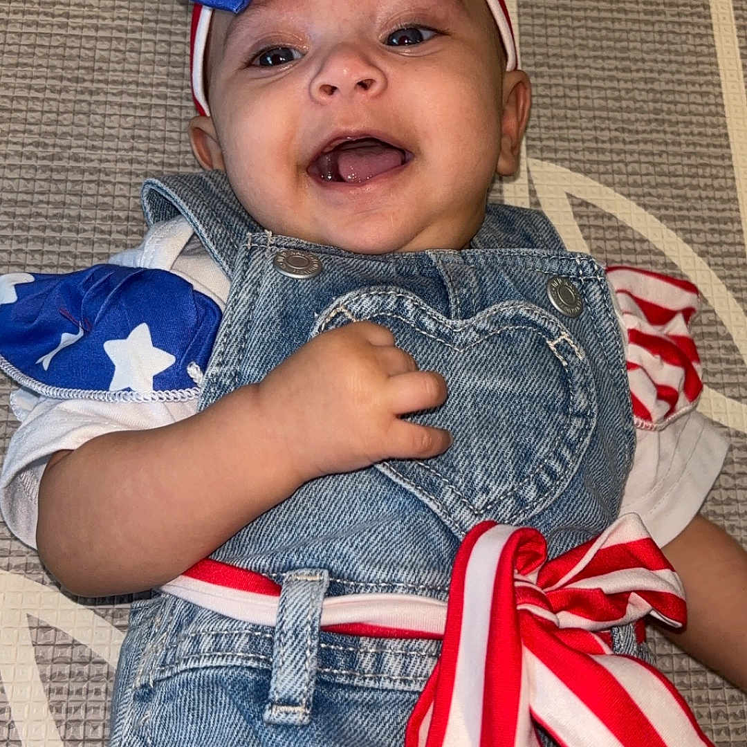 Amara is registered to the contest to win money with this photo: baby, baseballcap, cap, clothing, coat, couch, face, flag, furniture, happy, hat, head, jacket, jeans, laughing, pants, person, photography, portrait, shorts