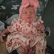 Savannah is registered to the contest to win money with this photo: baby, sleeping, pink_dress, headband, bow, floral_pattern, infant, peaceful, closeup, hand, feet, person, indoors, fabric, soft_lighting, cute, newborn, portrait, relaxation, child