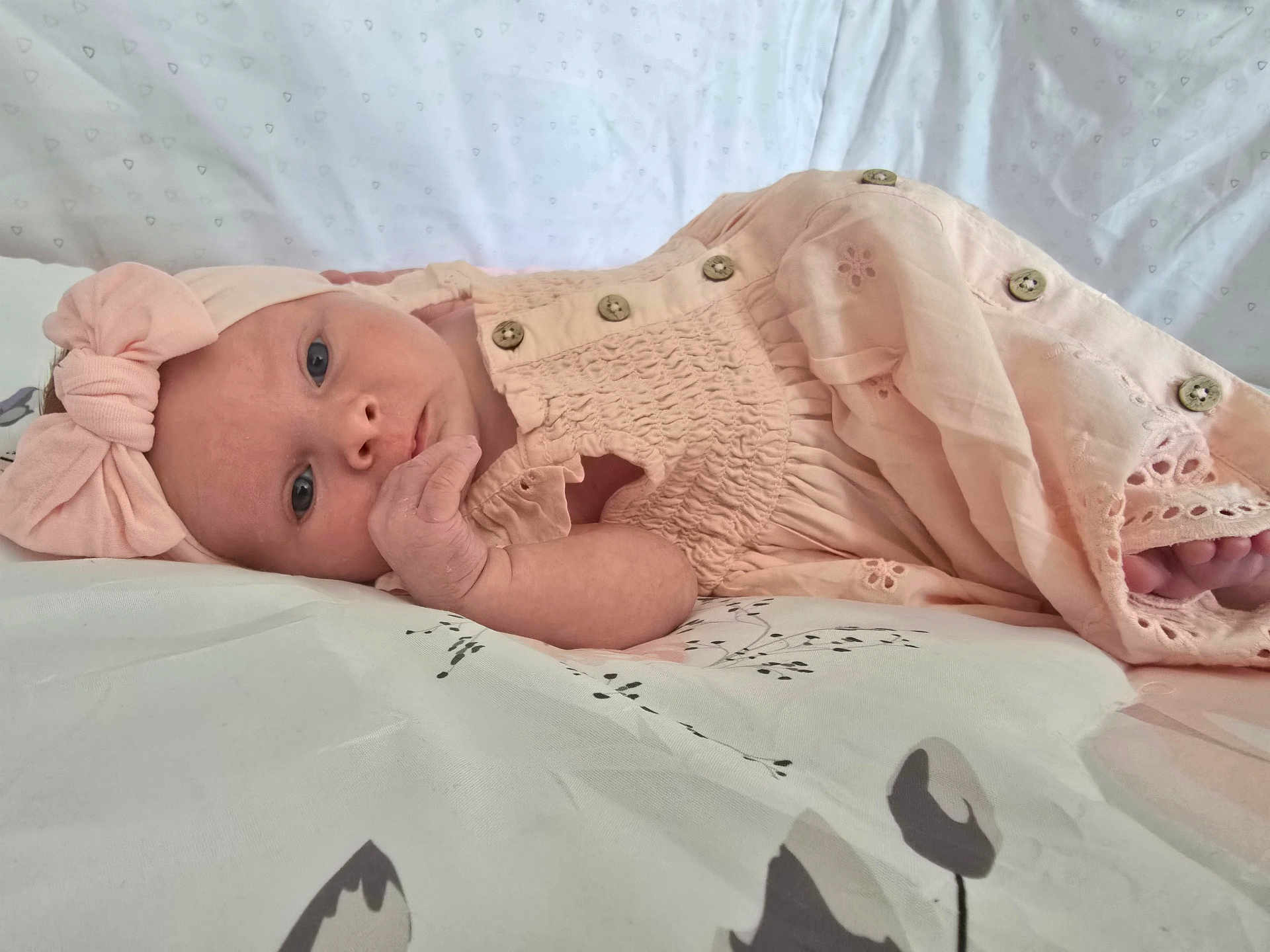 Savannah is registered to the contest to win money with this photo: baby, infant, bed, blanket, pink_clothing, headband, bow, hand, face, eyes, newborn, lying_down, soft_fabric, cute, child, sleepwear, pattern, fingers, portrait, indoors