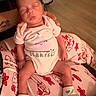 newborn, baby, sleeping, onesie, pink_clothing, hand, blanket, pattern, floor, person, infant, cute, cozy, soft_lighting, indoors, footwear, socks, tattoo, rest, peaceful