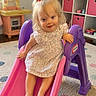 Sayler is registered to the contest to win money with this photo: toddler, child, slide, playroom, pink_bow, dress, toy_kitchen, colorful, indoor, carpet, smiling, play, furniture, storage_bins, happy, person, footwear_free, hair_accessory, cute, young_child