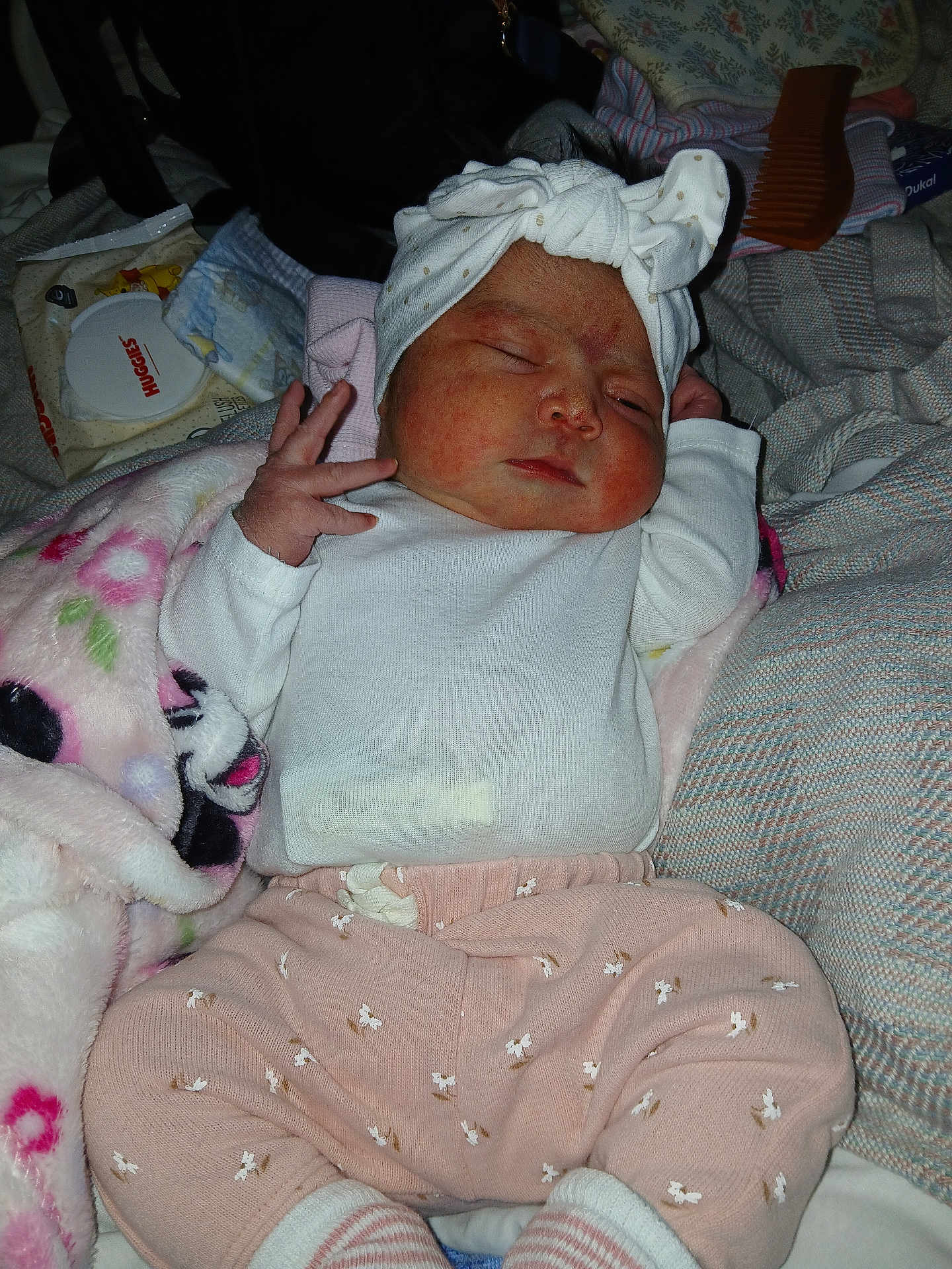 Jenesis is registered to the contest to win money with this photo: baby, infant, sleeping, headband, white_clothing, pink_pants, blanket, soft_toys, hand, face, newborn, indoor, cozy, couch, striped_socks, patterned_fabric, diaper_wipes, comb, resting, cute