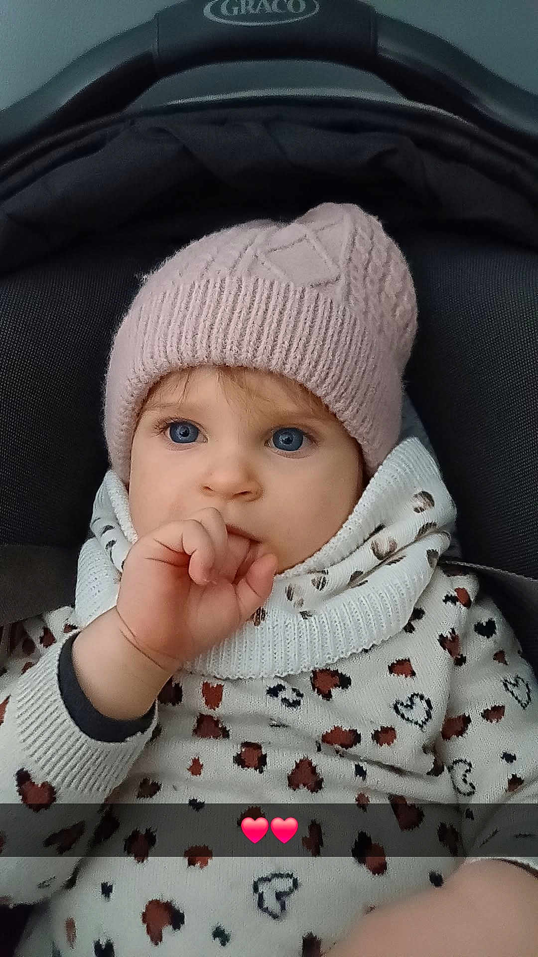 Charlie a rejoint le concours — aidez-le/la à gagner de superbes lots ! baby, child, blue_eyes, knitted_hat, pink_hat, thumb_sucking, car_seat, heart_pattern, sweater, cute, portrait, indoor, warm_clothing, infant, young_child, face, person, closeup, expression, seated