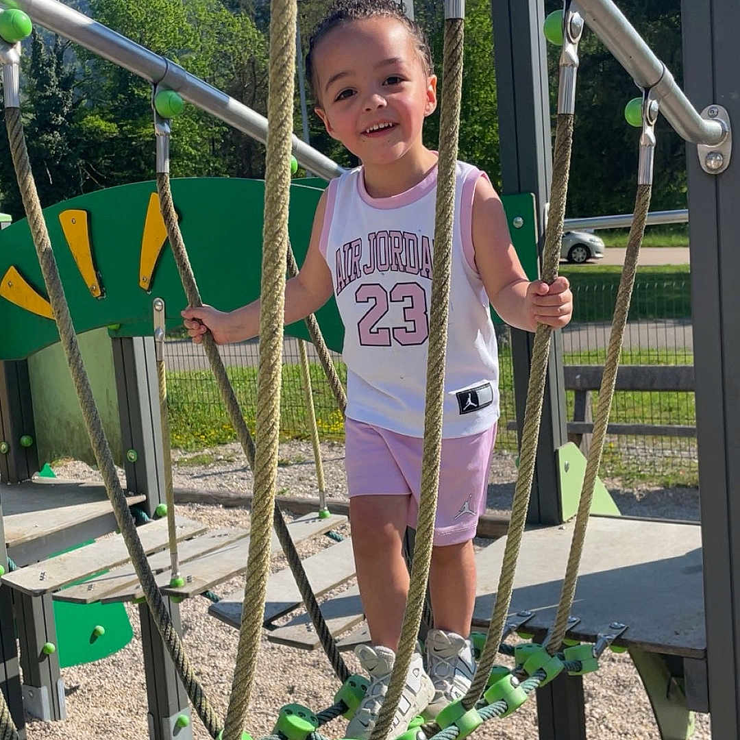Nawël a rejoint le concours — aidez-le/la à gagner de superbes lots ! air_jordan, bench, child, daylight, fence, gravel, happy, metal_bars, mountains, outdoor, person, playground, rope, rope_bridge, shorts, smiling, sneakers, sporty_clothing, summer, trees