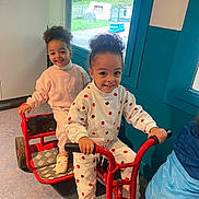 Nawël participe au concours pour gagner de l'argent avec cette photo : child, children, clothing, curly_hair, floor, friends, fun, greenery, happy, indoor, person, play, playtime, red, smile, sneakers, toddler, toy, tricycle, window