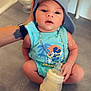 baby, child, mickey_mouse, blue_clothing, cap, bottle, milk, sitting, hand, tattoo, floor, tile, chain, cute, indoors, portrait, person, headwear, infant, support