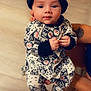 baby, child, infant, person, clothing, onesie, hat, indoor, floor, hand, tattoo, cute, calm, curious, sitting, holding, adult, sportswear, brooklyn_nets, portrait