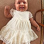baby, infant, smiling, white_dress, lace, cute, lying_down, cheeks, tongue_out, woven_basket, cushion, happy, child, adorable, soft_lighting, indoor, portrait, person, clothing, cute_face
