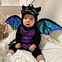 Leya joined the competition — help win amazing prizes! baby, child, costume, dragon, purple, black, wings, bed, blanket, teddy_bear, soft_toys, indoors, cute, sitting, white_socks, expression, face, headwear, plush, curtains