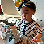 Leya joined the competition — help win amazing prizes! bottle, cafe, child, cup, curious, earrings, expression, face, headband, indoor, lemon_accessory, marble_table, natural_light, portrait, shadow, sitting, striped_clothing, table, toddler, water_bottle