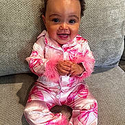 Alanna is registered to the contest to win money with this photo: baby, bows, child, clothing, couch, cute, fabric, face, feathers, hands, happy, indoor, infant, pajamas, pink, portrait, sitting, smile, texture, young_child
