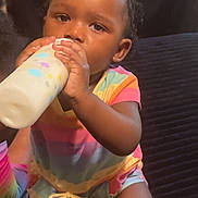 Ayla is registered to the contest to win money with this photo: toddler, child, baby, drinking, milk_bottle, colorful_clothing, striped_outfit, curly_hair, indoors, sitting, person, face, hand, milk, cute, young_child, portrait, infant, skin, expression